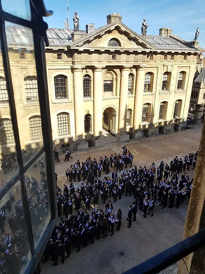 A picture looking out a window above a long line of students in their graduation gowns.